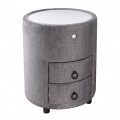 Designový čalouněný kulatý noční stolek Aluro s šedým potahem ze sametu se dvěma zásuvkami a nízkými černými nožičkami s bílou vrchní deskou s LED podsvícením