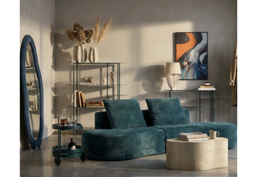 Moderní designová sestava nábytku do obývacího pokoje v tmavé tyrkysové barvě se sedačkou organického tvar a asymetrickým zrcadlem s knihovnou a konzolovým stolkem s oválnými policemi s kulatým servírovacím stolkem a konferenčním stolkem z kameniny v šedé barvě atypického