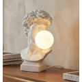 Moderní klasická bílá stolní lampa Antica s motivem Michelangelovy busty Davida s kulatým stínítkem umístěným v ústech připomínajícím žvýkačkovou bublinu