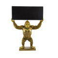Designová art deco stolní lampa Tierra Glam se zlatou podstavou ve tvaru stojící opice s roztaženýma rukama držící obdélníkové textilní stínítko v černé barvě