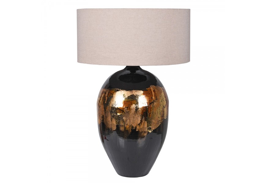 Designová art deco stolní lampa Manda s černou kovovou oblou nohou se zlatými a měděnými detaily a béžovým válcovým stínítkem ze lněného potahu