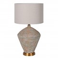 Designová vintage stolní lampa Tarragona s mohutnou podstavou z betonu ve světle béžové barvě s vyřezávaným geometrickým zdobením a patinou v odstínech červené a modré na zlatém kovovém podstavci s kulatým stínítkem ze lnu v naturální bílé krémové barvě