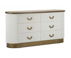 Designová glamour oválná komoda Glamia Blanc v bílé barvě se svislým žebrovaným zdobením se šesti zásuvkami s půlkruhovými úchyty a podstavou v metalickém bronzovém provedení a vrchní deskou v naturální hnědé barvě dřeva