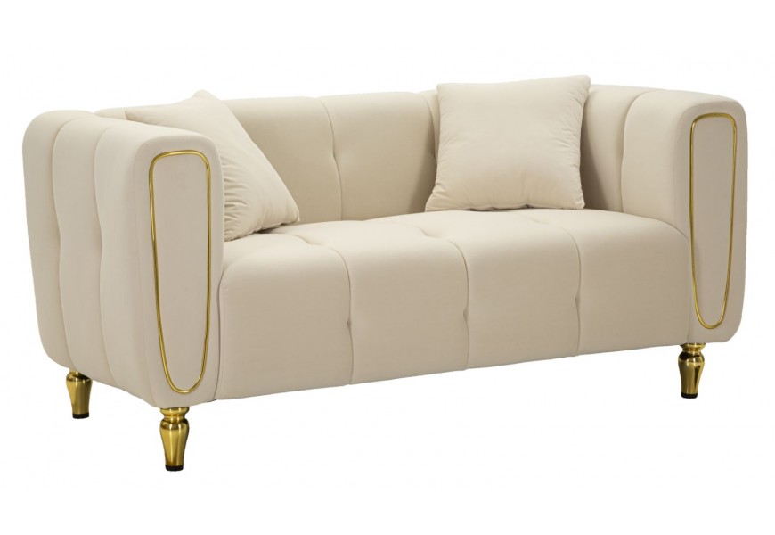 Designová art deco dvousedačka Celestia s textilním potahem v béžové barvě s kovovými ozdobnými prvky na opěrce a kovovými tvarovanými nožičkami ve zlaté barvě se dvěma polštáři a mohutnou lineární siluetou