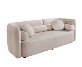 Art deco béžová třímístná sedačka Jina s potahem z bouclé látky s oblým asymetrickým opěradlem a geometrickými kulatými a válcovitými polštáři