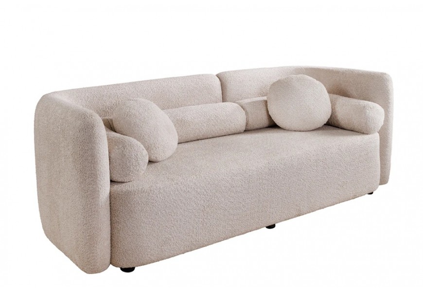 Art deco béžová třímístná sedačka Jina s potahem z bouclé látky s oblým asymetrickým opěradlem a geometrickými kulatými a válcovitými polštáři