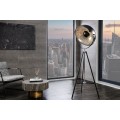 Industriální stojací lampa na trojnožce s velkým kovovým stínítkem ve tvaru reflektoru a černo-stříbrnou povrchovou úpravou v retro technickém stylu