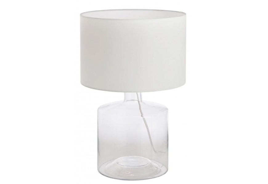 Moderní stolní lampa s bílým válcovým textilním stínítkem a průhledným skleněným podstavcem ve tvaru láhve s viditelným kabelem uvnitř