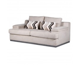 Luxusn&iacute; retro b&eacute;žov&aacute; sedačka Miranda pro dvě osoby s plnou podstavou s &scaron;ed&yacute;m dřevěn&yacute;m lemem s hranat&yacute;mi bočn&iacute;mi a z&aacute;dov&yacute;mi opěrkami a dvěma akcentov&yacute;mi pol&scaron;t&aacute;ři s chevronov&yacute;m vzorem s čern&eacute; a zemit&yacute;ch hněd&yacute;ch barv&aacute;ch